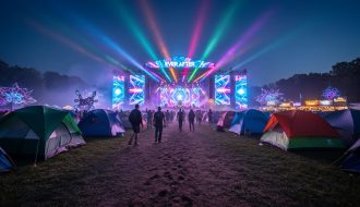 “Nighttime view of a lit EDM festival stage with neon light beams and silhouetted attendees walking through a camping area between installations.”